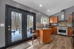 kitchen with wall chimney exhaust hood, brown cabinets, a breakfast bar, a peninsula, and high end stove