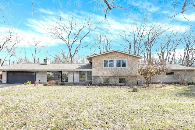 split level home with a garage, stone siding, a front yard, and driveway