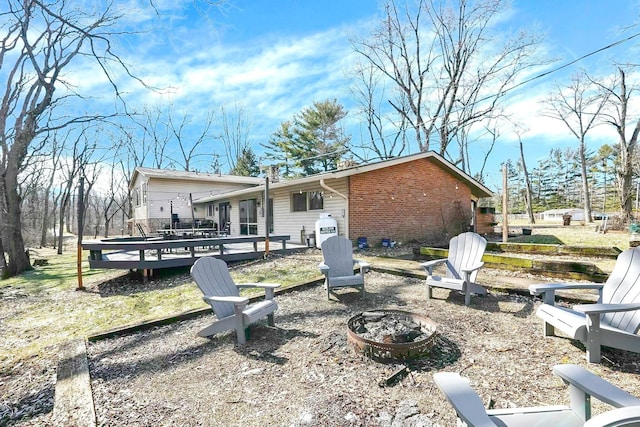 back of property featuring an outdoor fire pit, a deck, and brick siding