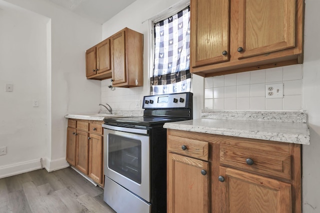 kitchen featuring sink, light hardwood / wood-style flooring, stainless steel electric stove, light stone countertops, and decorative backsplash