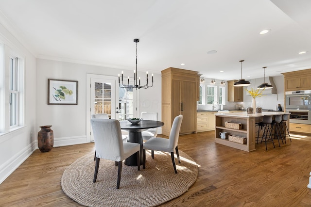 dining area with hardwood / wood-style flooring, crown molding, sink, and a notable chandelier