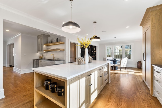 kitchen featuring a kitchen island, pendant lighting, stainless steel microwave, ornamental molding, and light wood-type flooring