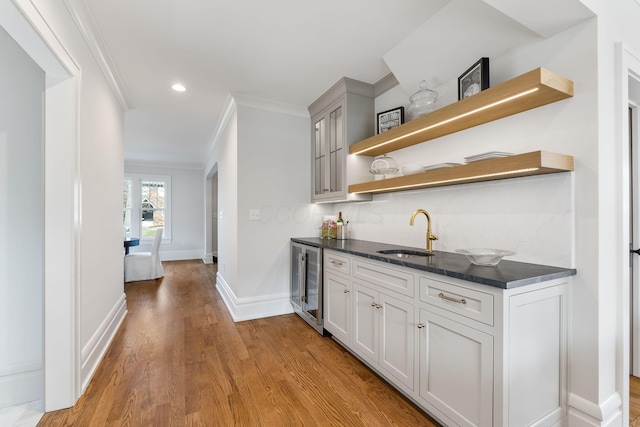 bar with wine cooler, sink, ornamental molding, light hardwood / wood-style floors, and white cabinets