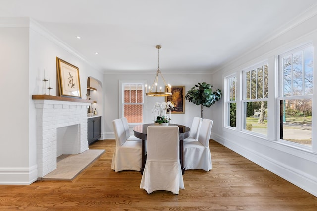 dining space with hardwood / wood-style flooring, crown molding, a chandelier, and a brick fireplace