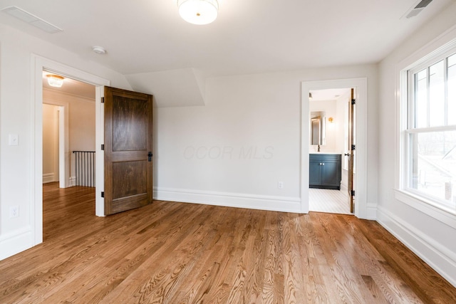 unfurnished bedroom with lofted ceiling, connected bathroom, and light hardwood / wood-style floors