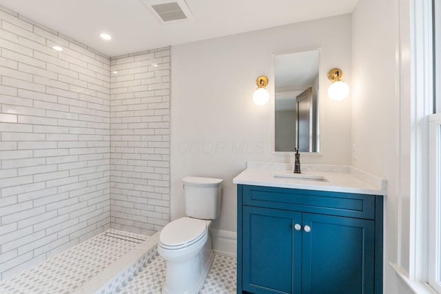 bathroom featuring vanity, a tile shower, and toilet