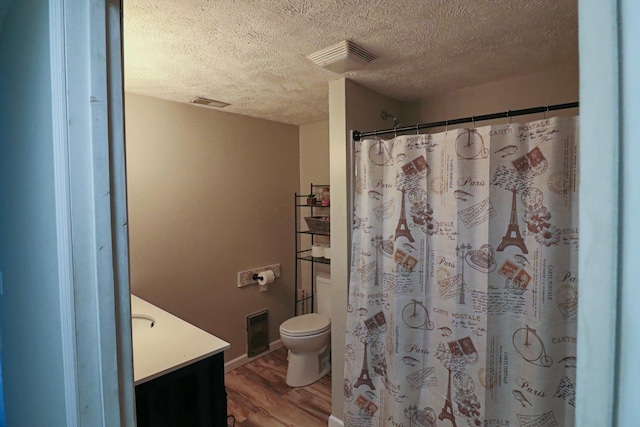 bathroom with heating unit, wood-type flooring, vanity, toilet, and a textured ceiling