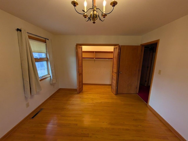 unfurnished bedroom with a notable chandelier, light hardwood / wood-style floors, and a closet