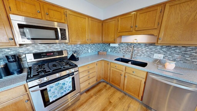 kitchen with appliances with stainless steel finishes, sink, decorative backsplash, and light hardwood / wood-style flooring