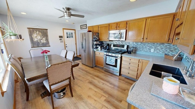 kitchen with sink, ceiling fan, appliances with stainless steel finishes, light hardwood / wood-style floors, and decorative backsplash