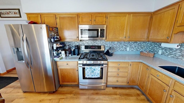 kitchen with stainless steel appliances, sink, light hardwood / wood-style floors, and decorative backsplash