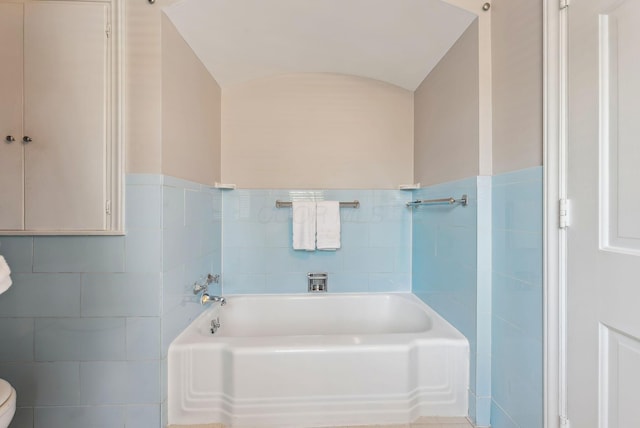 bathroom with tile walls, a tub to relax in, and toilet