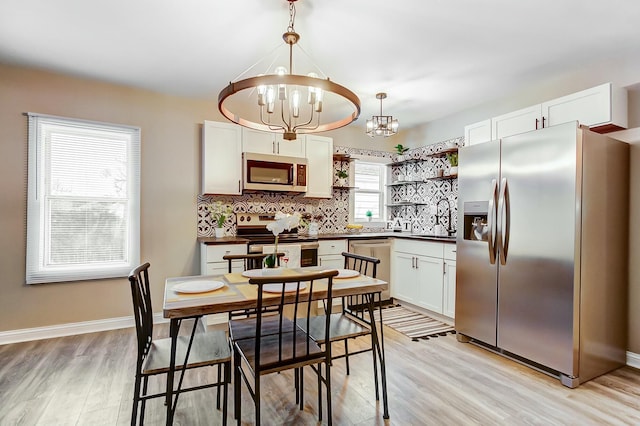 kitchen featuring white cabinetry, a chandelier, pendant lighting, stainless steel appliances, and backsplash