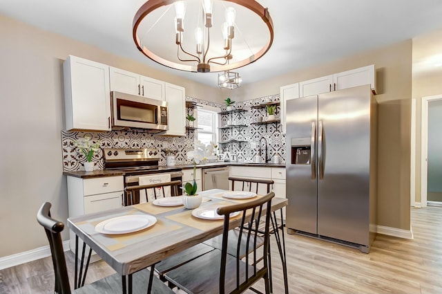 kitchen featuring pendant lighting, appliances with stainless steel finishes, white cabinetry, a notable chandelier, and decorative backsplash