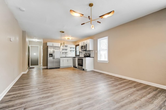 kitchen featuring appliances with stainless steel finishes, pendant lighting, light hardwood / wood-style floors, decorative backsplash, and white cabinets