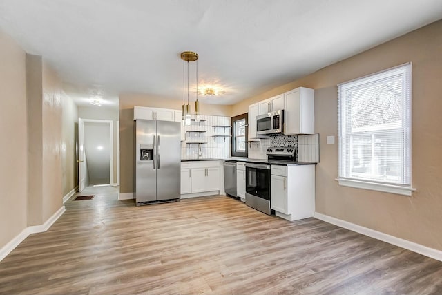 kitchen with appliances with stainless steel finishes, tasteful backsplash, white cabinetry, hanging light fixtures, and light hardwood / wood-style floors