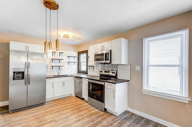 kitchen with sink, appliances with stainless steel finishes, hanging light fixtures, white cabinets, and decorative backsplash