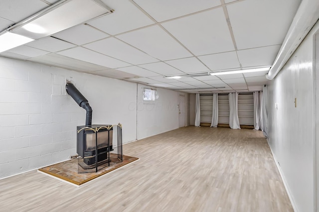 basement featuring a paneled ceiling, wood-type flooring, and a wood stove