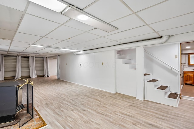 basement featuring a paneled ceiling, light hardwood / wood-style floors, and a wood stove