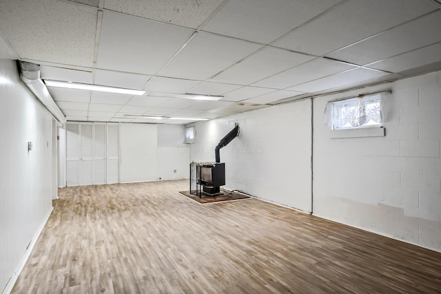 basement featuring wood-type flooring, a wood stove, and a drop ceiling