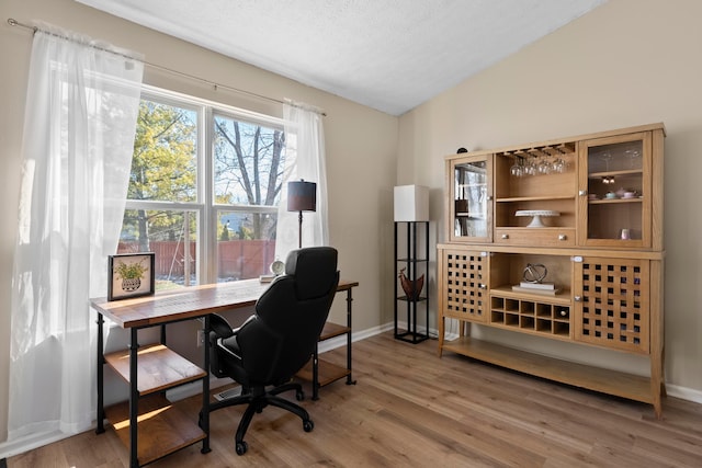 home office with lofted ceiling, hardwood / wood-style floors, and a textured ceiling