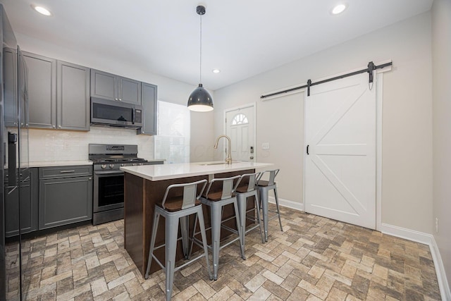 kitchen with sink, hanging light fixtures, stainless steel appliances, a barn door, and a center island with sink