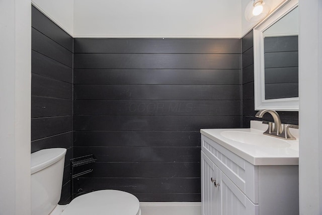 bathroom featuring vanity, toilet, and wood walls