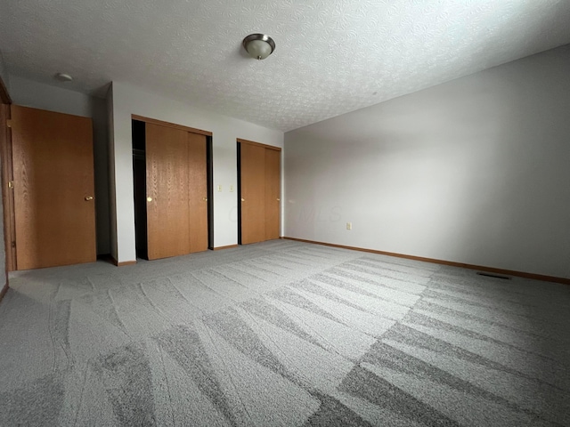 unfurnished bedroom featuring multiple closets, light colored carpet, and a textured ceiling