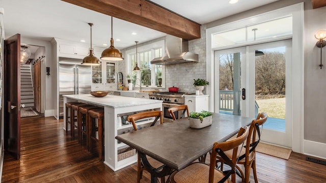 kitchen with high quality appliances, light countertops, dark wood-style floors, white cabinetry, and wall chimney exhaust hood