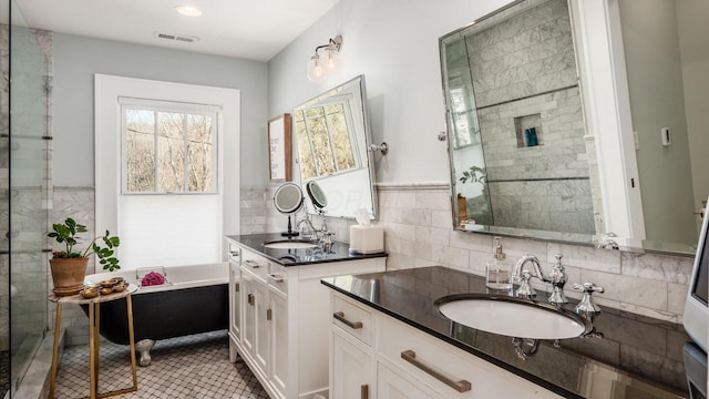 full bathroom with two vanities, a bath, visible vents, and a sink