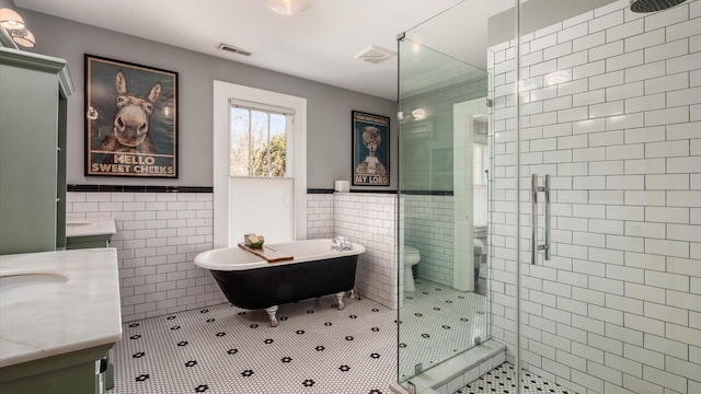 bathroom with tile patterned floors, visible vents, a stall shower, tile walls, and vanity