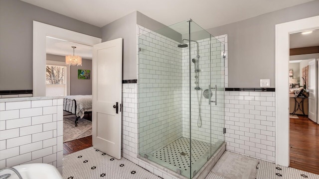 ensuite bathroom with wood finished floors, a stall shower, ensuite bathroom, wainscoting, and tile walls