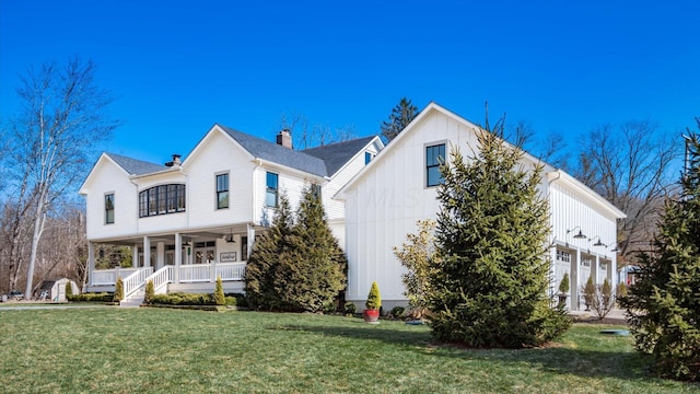 modern farmhouse with a porch, a chimney, a front lawn, a garage, and board and batten siding