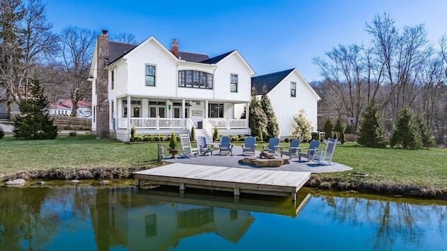 rear view of property with a water view, a fire pit, a chimney, and a lawn