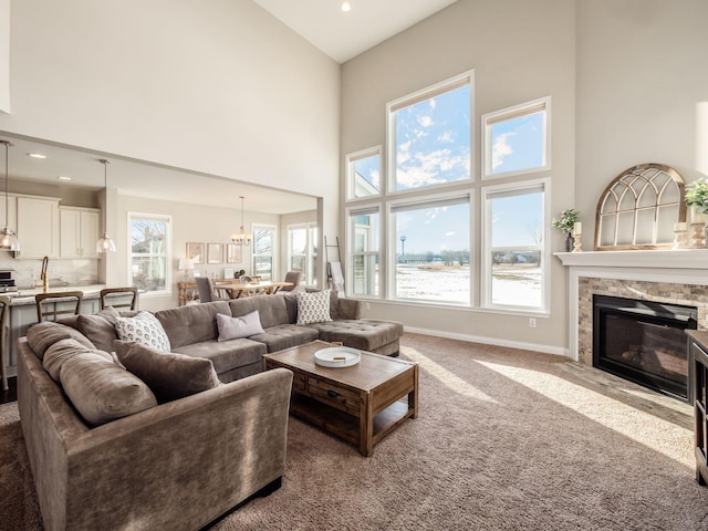 living room featuring a towering ceiling, a stone fireplace, a chandelier, and carpet