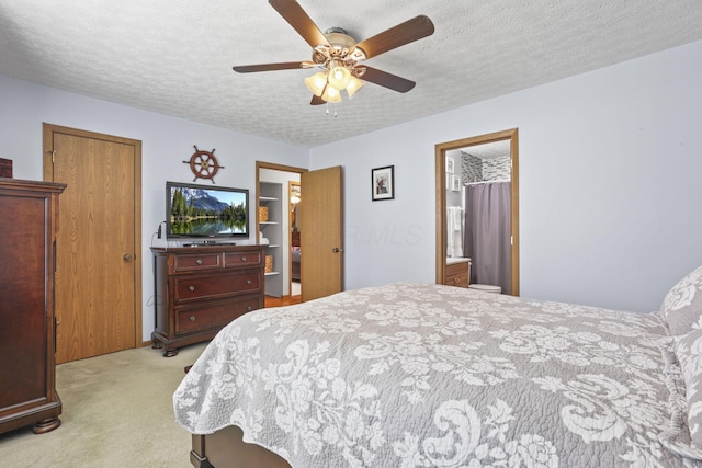 bedroom featuring ceiling fan, connected bathroom, light colored carpet, and a textured ceiling