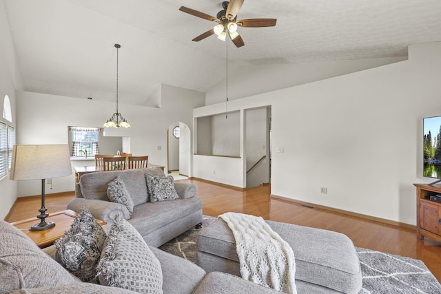 living room with hardwood / wood-style floors, ceiling fan with notable chandelier, and vaulted ceiling