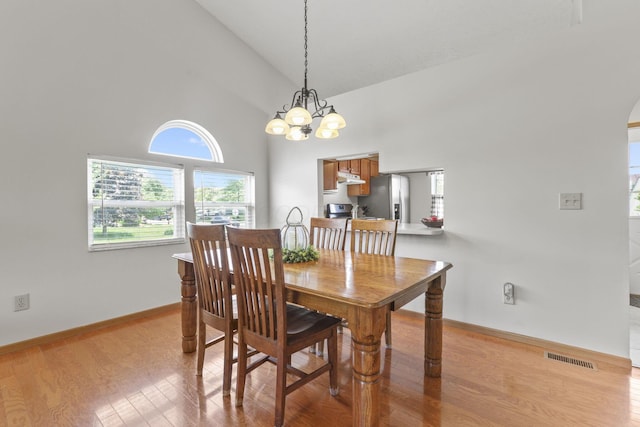 dining room with an inviting chandelier, light hardwood / wood-style flooring, and high vaulted ceiling