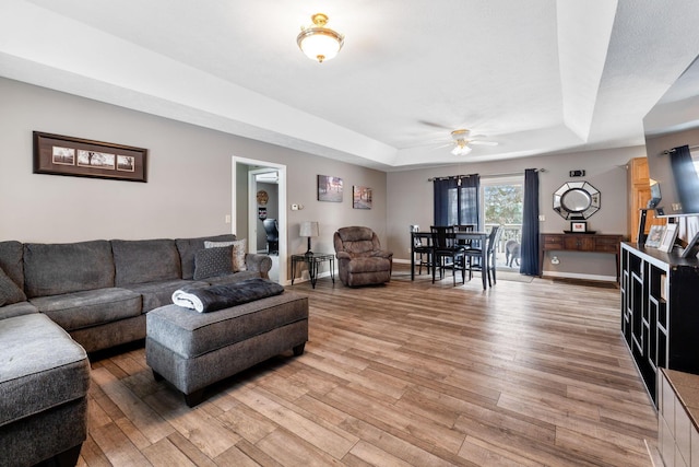 living room with ceiling fan, baseboards, a raised ceiling, and wood finished floors