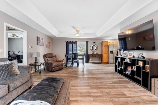 living area featuring a ceiling fan, a tray ceiling, and light wood finished floors