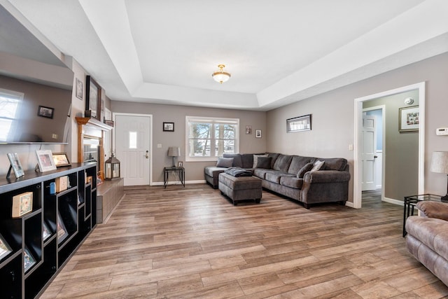 living area featuring a tray ceiling, baseboards, and light wood finished floors