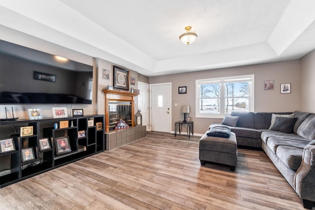 living area with a tray ceiling, a tile fireplace, wood finished floors, and baseboards