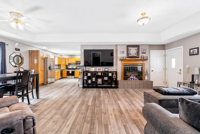 living room featuring light wood-style flooring, a fireplace, and a raised ceiling