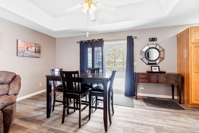 dining room with light wood finished floors, ceiling fan, baseboards, and a raised ceiling