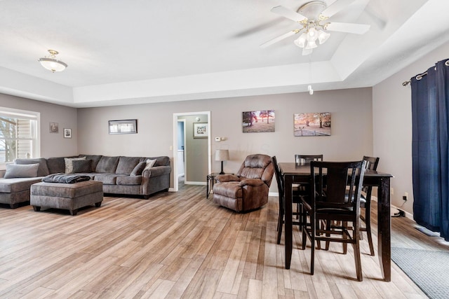 living area with light wood finished floors, a raised ceiling, a ceiling fan, and baseboards