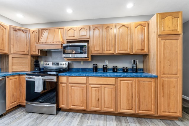 kitchen featuring stainless steel appliances, dark countertops, custom range hood, and light wood finished floors