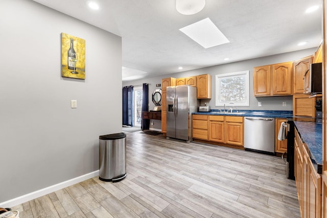 kitchen with dark countertops, a skylight, light wood-type flooring, and stainless steel appliances