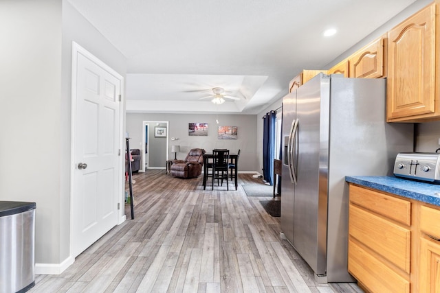 kitchen featuring light wood-type flooring, stainless steel fridge with ice dispenser, light brown cabinetry, dark countertops, and a raised ceiling