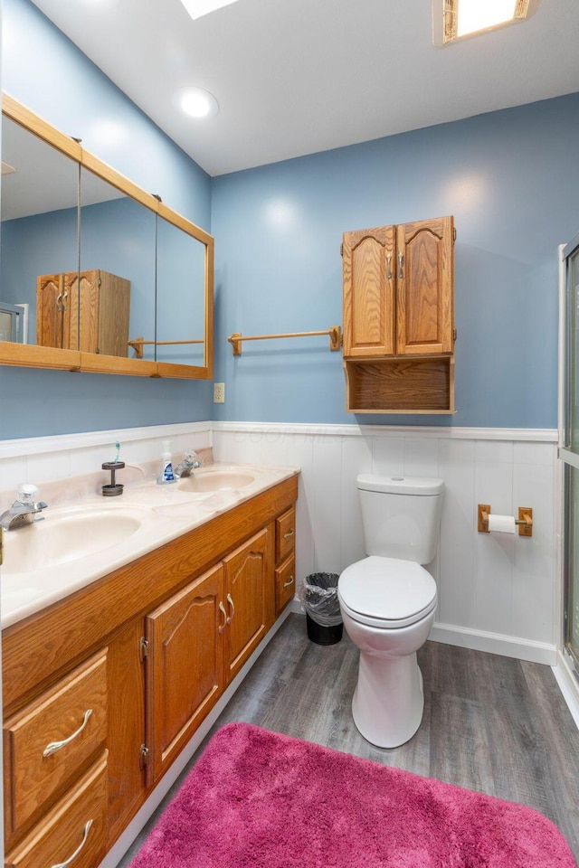 full bath with double vanity, wood finished floors, wainscoting, and a sink