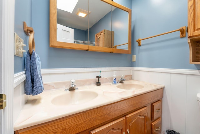 bathroom featuring wainscoting, a sink, toilet, and double vanity